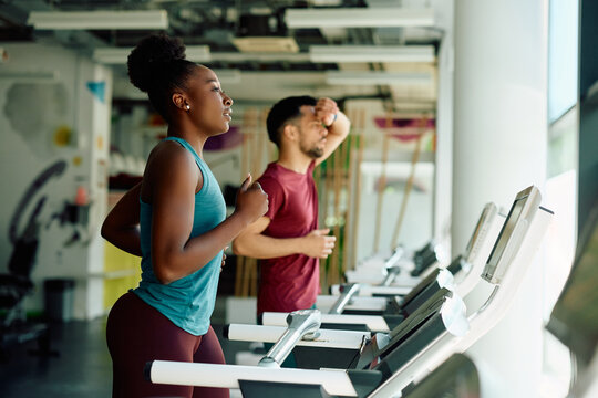 Young black sportswoman running on treadmill during sports training in gym.