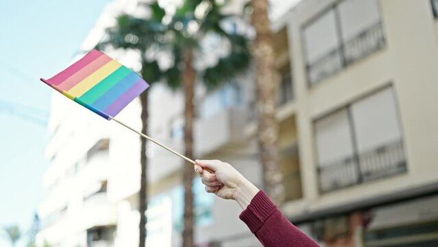 Young hispanic man holding rainbow flag at street