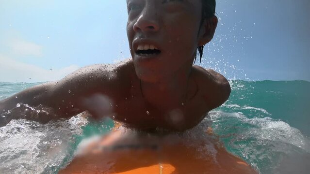 Asian surfer getting barreled on the surf. Blue ocean and scenic landscape at background. Powerful ocean and one man alone do workout with surf barreled at big waves. POV by gopro