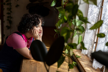 Obraz na płótnie Canvas Portrait of a smiling brunette girl twenty-five years old dressed in a vintage pink blouse and blue velvet jumpsuit looks out the window in a cafe.