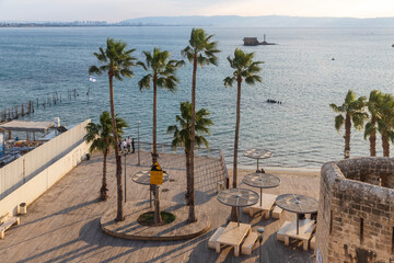Naklejka premium Acre, Israel - January 08, 2023: Sunset view of the Horses beach, the sea wall and the fishing port, with locals and visitors, in the old city of Acre (Akko), Israel