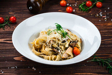 Pasta Tagliatelle with chicken, tomatoes, mushrooms, parmesan cheese and greens in a plate.