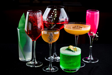 Set of various multi-colored alcoholic cocktails in glasses on a dark background.