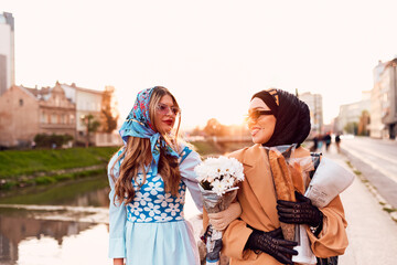 Couple woman one wearing a hijab and a modern yet traditional dress, and the other in a blue dress...