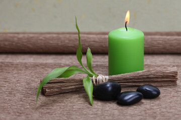 Obraz na płótnie Canvas Burning green candle, black stones and bamboo leaf on brown mat background.