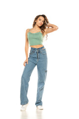 Fototapeta premium Full length shot of young woman wearing green shirt and blue jeansi while standing at isolated white background.