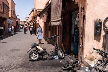 A scooter garage with a broken scooter in front, a female tourist walking along the alley