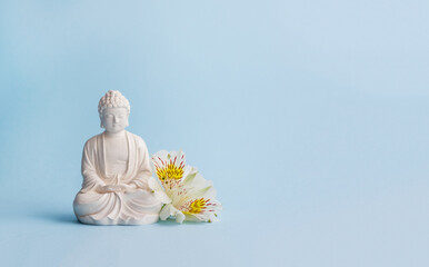 Vesak Day is holy day for Buddhists. Happy Buddha Day with Siddhartha Gautama statue with white flowers on blue background. Mental health and meditation concept. Selective soft focus, copy space