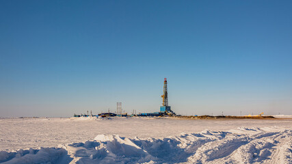 A gas field in the Arctic. Polar winter day. In the foreground is a snowy tundra. In the background is a drilling rig and industrial infrastructure © mangz