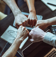Symbol of unity within business team. Members of team form circle, raising fists in gesture of...