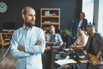 Manager's portrait against backdrop of focused business team working together to find solutions or discuss goals. Manager's presence exudes confidence and leadership, guiding team towards success