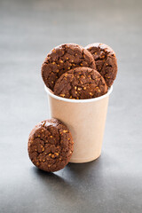 Cocoa oatmeal cookies with crushed peanuts. In a paper cup. Dark gray background