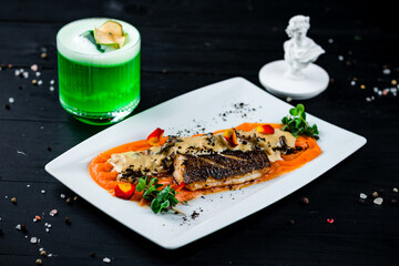 Fried white fish with carrot puree, mushrooms in sauce, truffles, microgreens with green cocktail.