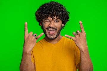 Overjoyed young indian man showing rock n roll gesture by hands, cool sign, shouting yeah with...