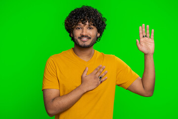 I swear to be honest. Sincere responsible young indian man raising hand to take oath, promising to be honest and to tell truth, keeping hand on chest. Hindu guy isolated on green chroma key background