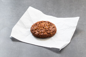Cocoa oatmeal cookie with crushed peanuts. On paper. Dark gray background. Close up