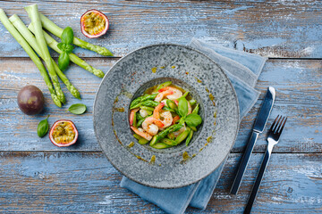 Grüner Spargel Salat gedämpft als Spitzen und Scheiben mit Garnelen und Passionsfrucht Vinaigrette serviert als Draufsicht auf einem Nordic Design Teller mit Textfreiraum