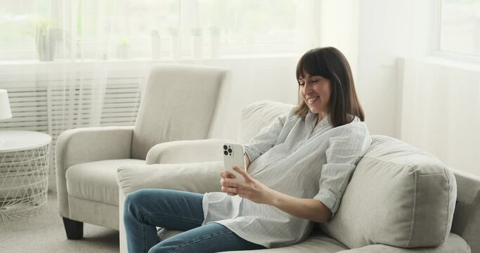 A Joyful Pregnant Caucasian Woman Captures A Special Moment On The Living Room Couch. With A Beaming Smile, She Takes A Selfie Using Her Phone, Cherishing This Beautiful Time In Her Life.