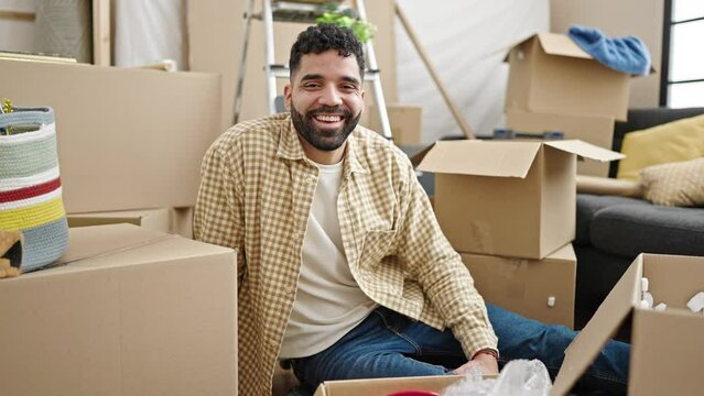 Young hispanic man smiling confident sitting on floor at new home