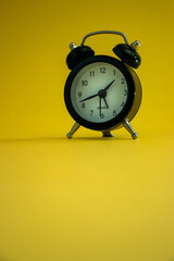 Small black alarm clock, black numbers, set the time placed on a table. Clock on isolated yellow