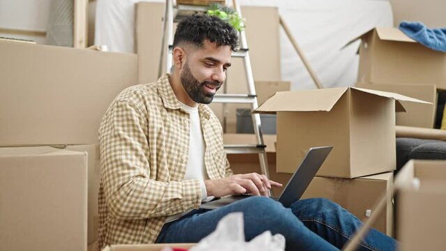 Young hispanic man using laptop sitting on floor at new home