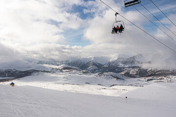 Fototapeta na wymiar Mounain range covered in snow and clouds over them with gondola car and skiers