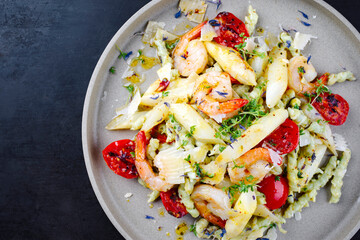 White asparagus glazed with fried king prawns and pistachio pasta served as a top view on a design plate with text space 