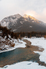 Snowy mountain peak at a cloudy sunset with a river flowing