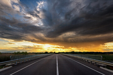 Empty asphalt highway outside the city, sunset with storm clouds