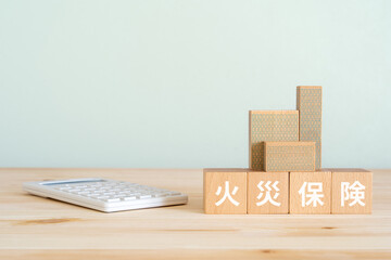 火災保険と書かれたブロック、電卓、ミニチュアの建物 © ELUTAS