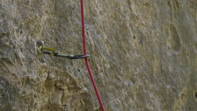 CLOSE UP, DOF: Bolt hanger with attached quickdraw and running climbing rope. Important climbing equipment to assure protection and safety of lead climber during adrenaline sport activity in verticals