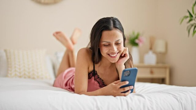 Young beautiful hispanic woman using smartphone lying on bed at bedroom