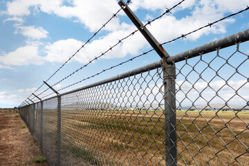 A long chain link fence with barbed wire stretches into istance - Powered by Adobe