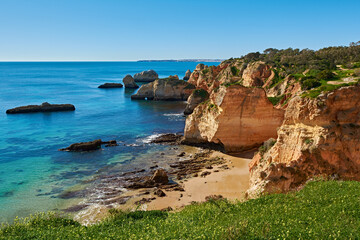 Solitary beach close to Alvor village in Portugal. There are lots of limestone rocks in the water and green grass in the foreground