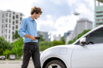 Progressive businessman insert charger plug from charging station to his electric vehicle with...