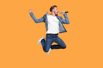 Fototapeta na wymiar Handsome man with microphone singing and jumping on yellow background