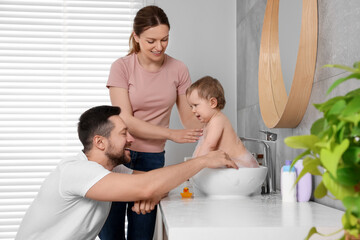 Father and mother washing their little baby in sink at home