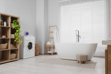 Stylish bathroom interior with beautiful tub, washing machine and decor elements