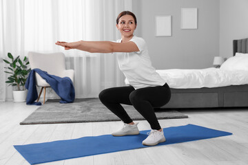 Fototapeta premium Morning exercise. Happy woman squatting at home