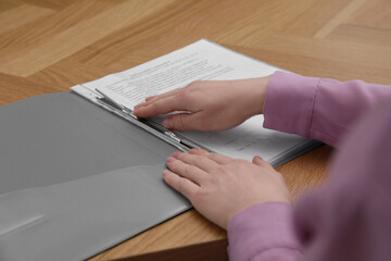 Woman fixing folder with punched pockets at wooden table, closeup