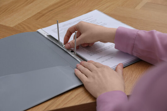 Woman fixing folder with punched pockets at wooden table, closeup