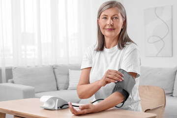 Woman measuring blood pressure at wooden table in room, space for text