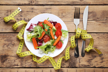 Plate with fresh vegetable salad and measuring tape on wooden table, flat lay. Healthy diet concept