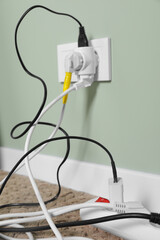 Different electrical plugs in socket and power strip on floor indoors, closeup