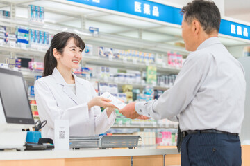 薬局で薬の相談を受ける高齢者男性と薬剤師・調剤師の女性

