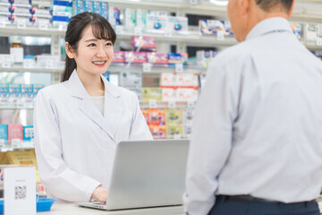 薬局でノートパソコンを使いながら相談を受ける薬剤師・調剤師
