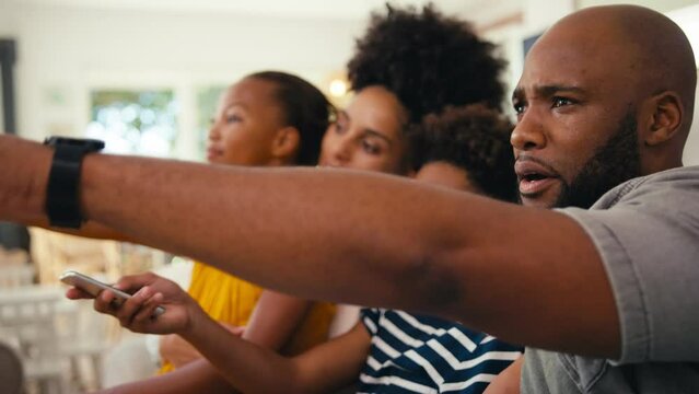 Family at home sitting on sofa together streaming show or movie to TV - shot in slow motion 