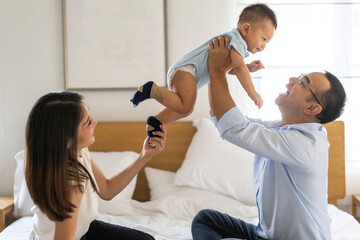 Portrait of enjoy happy love family asian father and mother playing with adorable little asian baby.newborn, infant.dad touching with cute son moments good time in a white bedroom.Love of family