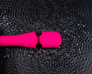 The pink dildo creates a vibration on the surface of the water. Sex toy on a black background.
