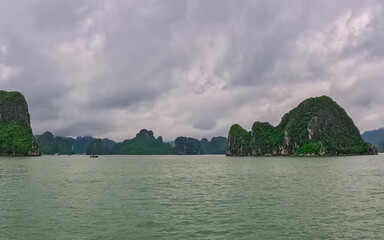 Fototapeta na wymiar Ha Long Bay littered with mountains and Rock cliffs popping out of the ocean, lush green mountains in Vietnam